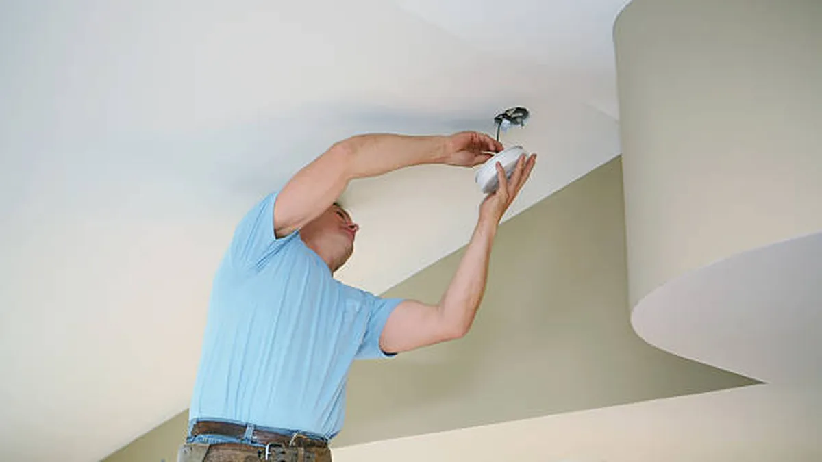 Electrician fitting a ceiling smoke alarm in a Sydney home — Bilgola Beach